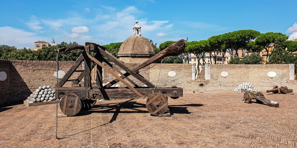 Catapulta reconstruida y bolas de cañón de piedra apiladas sobre las murallas del castillo de Sant’Angelo, con la cúpula de San Pedro al fondo, Roma