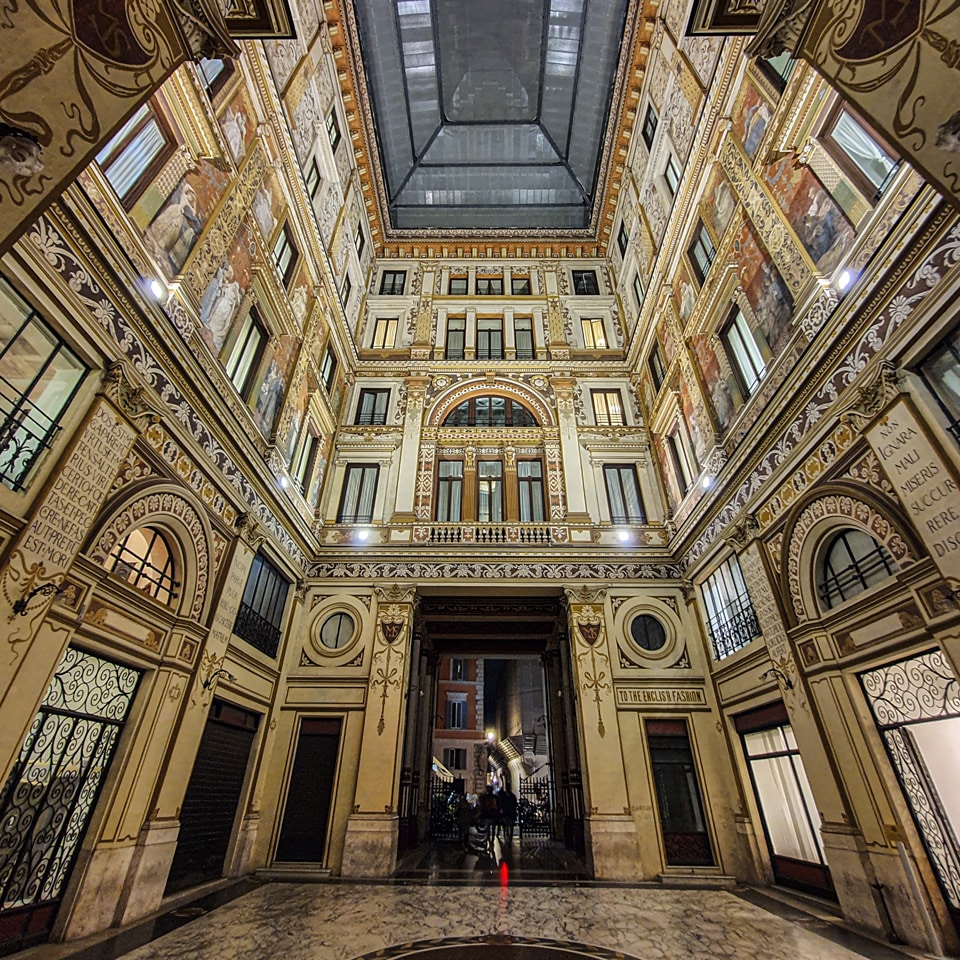Inscripción Non ignara mali de la Eneida en un pilar junto a un rótulo pintado de la tienda English Fashion en la Galleria Sciarra, Roma